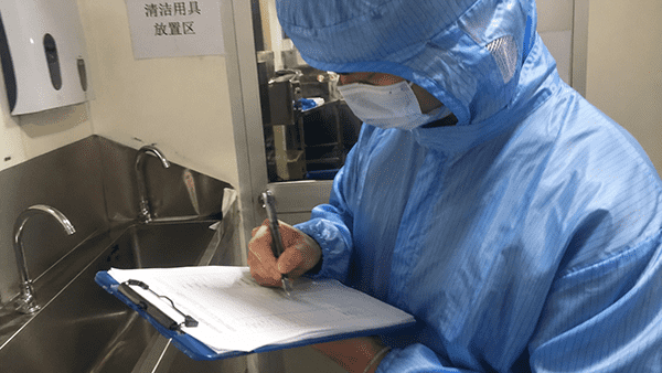 A person in a cleanroom suit holding a clipboard and inspecting a product, symbolizing rigorous quality control.