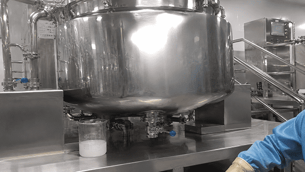 Lab Scale vs. Production Scale Manufacturing An image showing a small lab beaker next to a large stainless steel manufacturing tank to highlight the difference in scale.