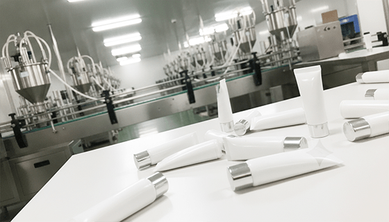 A cosmetic lab technician looking at beakers next to a production line, illustrating the professional manufacturing process.