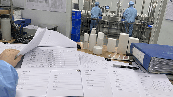 production planning sheet and technical documentation folder side by side on a factory desk, batch records and labelling drafts visible