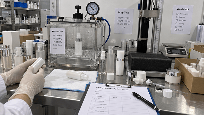 packaging seal-integrity test station with sample bottles in a vacuum chamber beside a drop-test rig, iPhone-angle snapshot